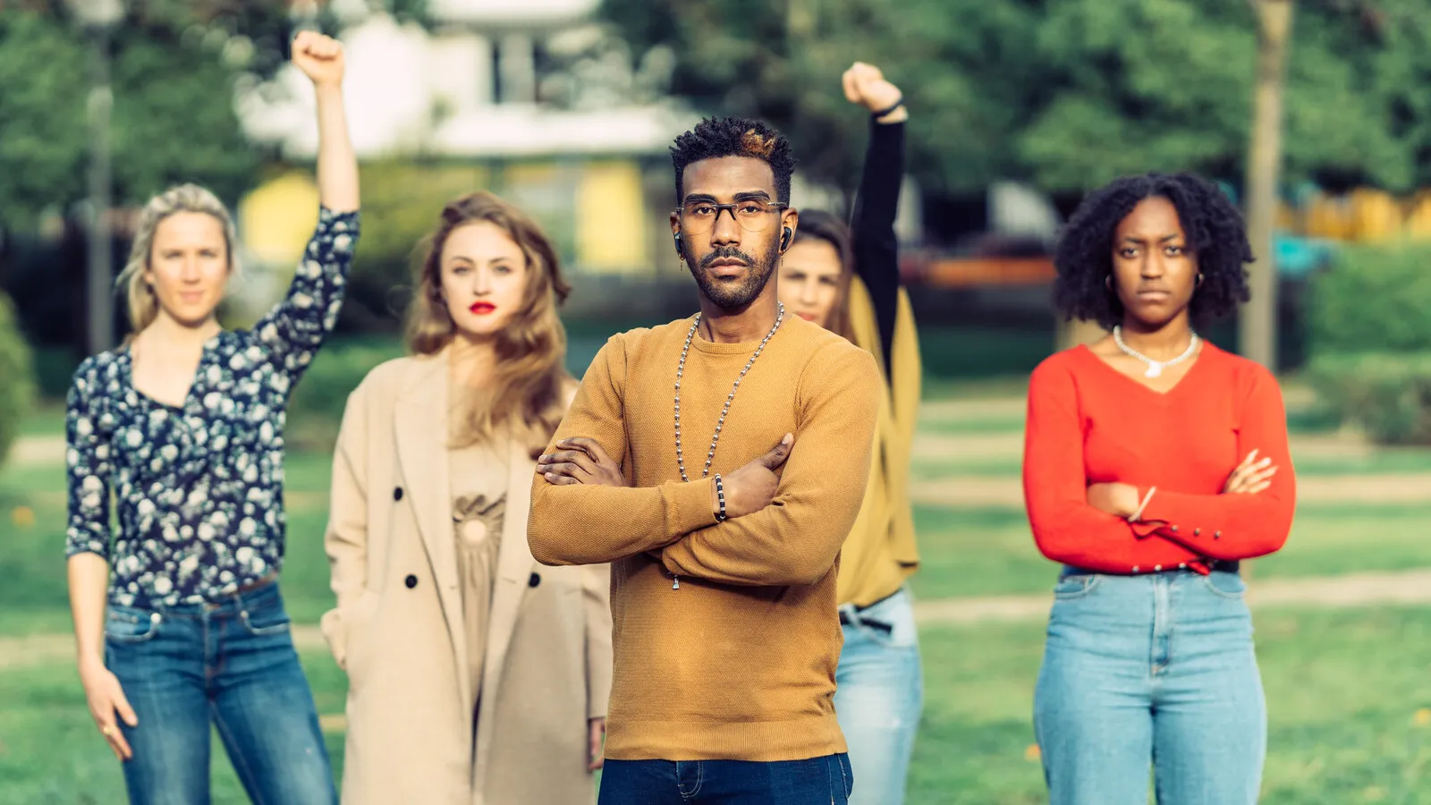 A group of people standing together outdoors with hands raised in solidarity, late-day sun lighting them from behind.
