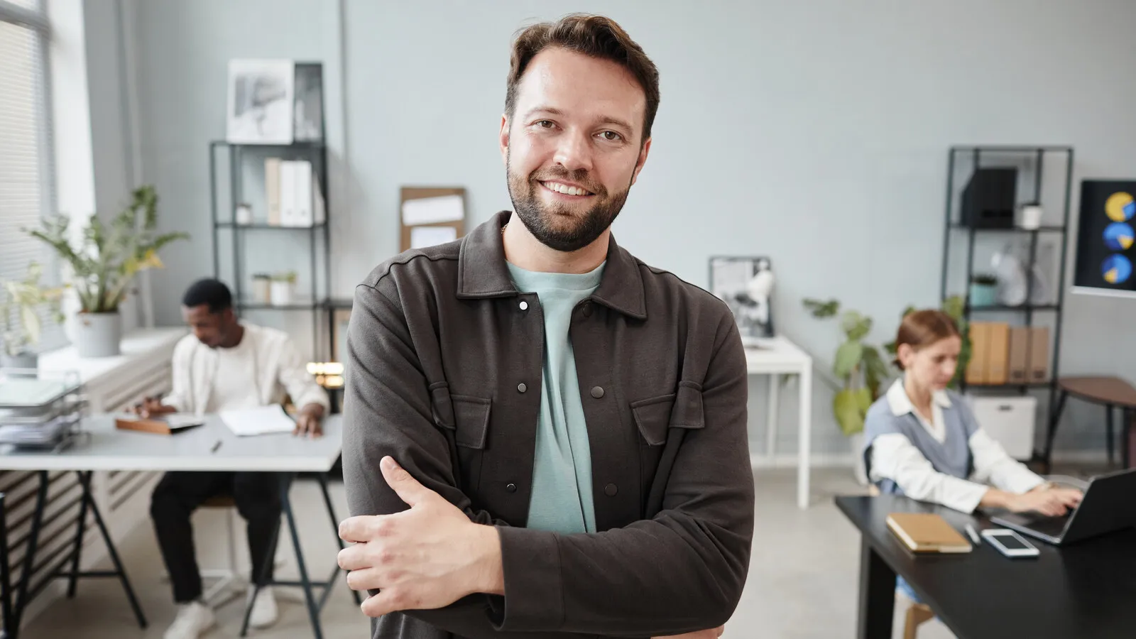 A young professional in an office setting, dressed for work, smiling confidently.