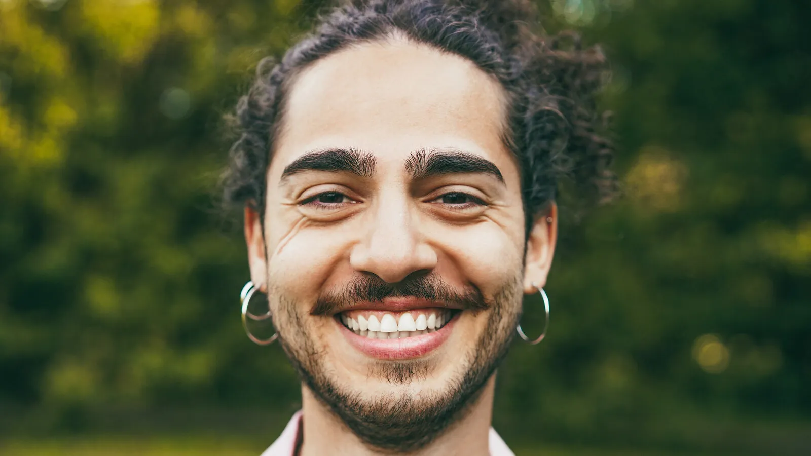 A young person with curly hair standing outdoors in soft natural light, expression open and at ease.