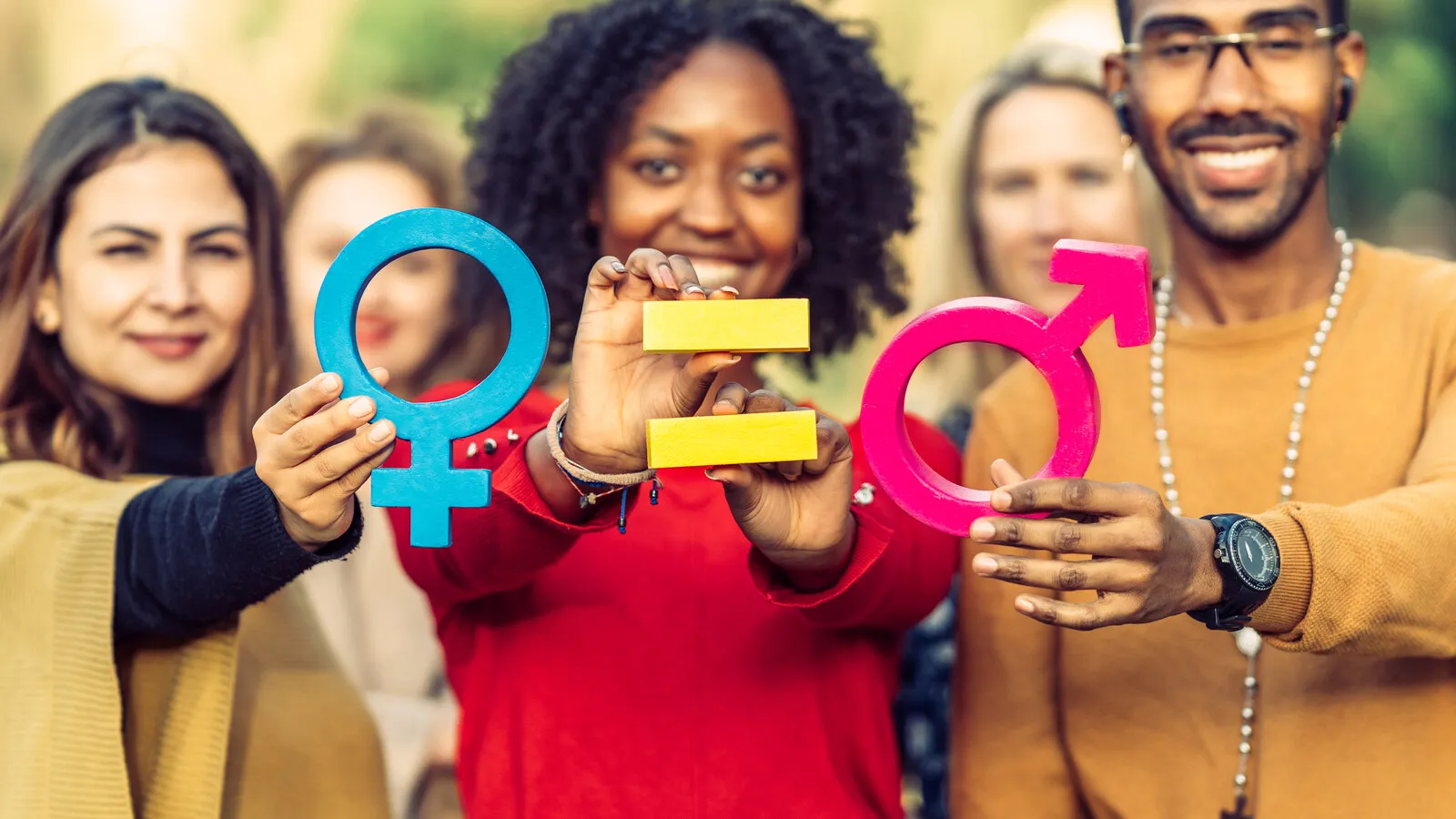 Hands gently holding small symbols representing gender identity and equality, rendered in warm tones.